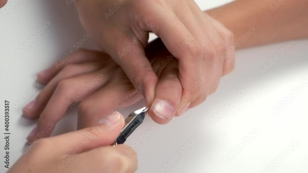 Woman is cutting skin around nail on teenager boy hand using nail tongs, hands closeup. Cuts off the burrs near the nails on white background. Hygiene procedure and care for hands. Woman is cutting skin around nail on teenager boy hand using nail tongs, hands closeup. Cuts off the burrs near the nails on white background. Hygiene procedure and care for hands.