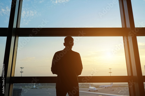 Silhouette of man coming to window to look at new airplanes on large air field in contemporary airport terminal backside view