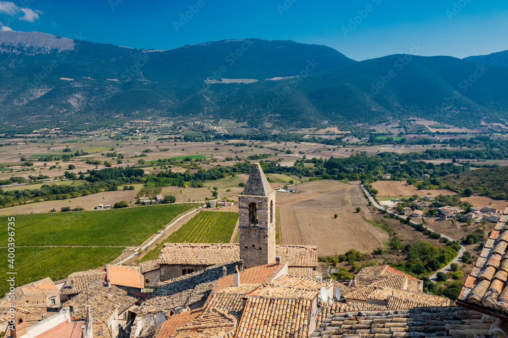 The ancient medieval village of Capestrano seen from the top of the castle. The tiled roofs of the houses, the bell tower, the valley with the cultivated fields and the green mountains in background.