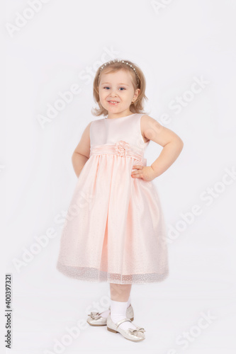 A beautiful little girl in a ball gown stands tall on a white background. The baby poses for the camera in the studio. Happy childhood. The concept of fashionable children s clothing