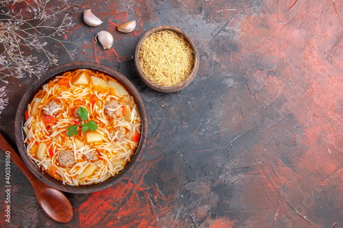 Above view of delicious noodle soup with chicken and uncooked pasta in a small brown bowl and spoon garlic on the dark background