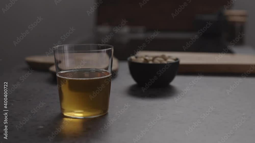 Slow motion handheld shot of apple cider in glass and pistachios in black bowl on concrete countertop Slow motion handheld shot of apple cider in glass and pistachios in black bowl on concrete countertop