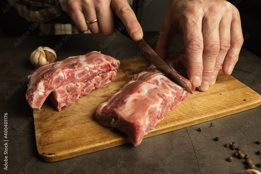 Men's hands cut fresh pork ribs. Cooking for frying with garlic, allspice on a wooden board, gray background.
