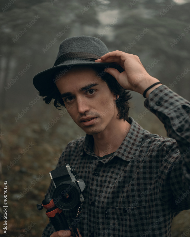 Obraz premium young man traveler in with a hat and a camera looking for adventure in a foggy forest