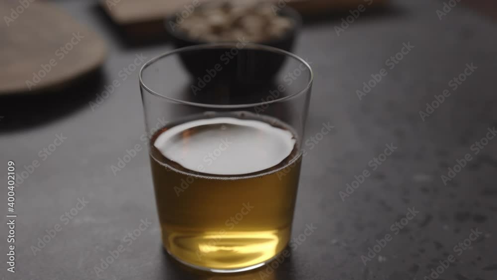 Slow motion handheld shot of apple cider in glass and pistachios in black bowl on concrete countertop Slow motion handheld shot of apple cider in glass and pistachios in black bowl on concrete countertop