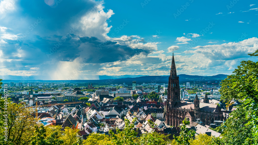Germany, Freiburg im Breisgau, Rain and thunderstorm in summer above skyline of the city and muenster church, aerial view above