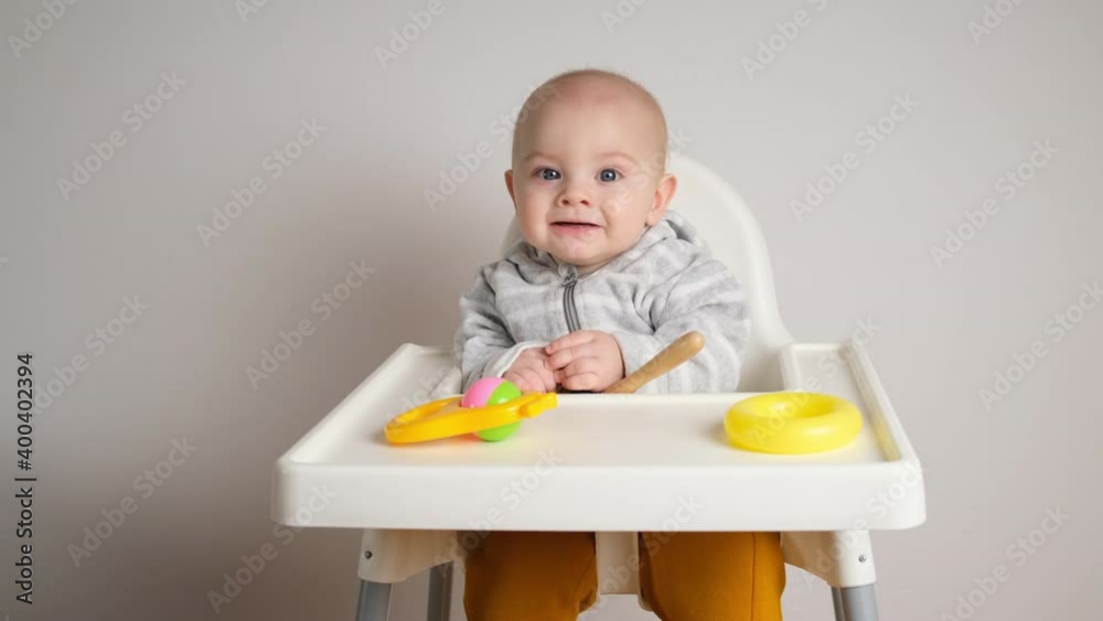 Little infant boy is talking sitting in baby high chair. Cute caucasian baby with plastic developing toys indoors. Little infant boy is talking sitting in baby high chair. Cute caucasian baby with plastic developing toys indoors.