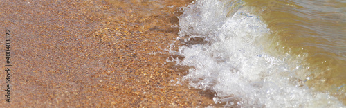 A sea wave with white foam runs over the yellow sand of the seashore.