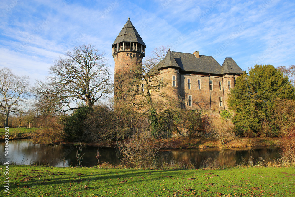 Panoramic view over moat on medieval ancient old german water castle and defensive tower from 12th century with bare trees in winter against blue sky - Krefeld Linn, Germany
