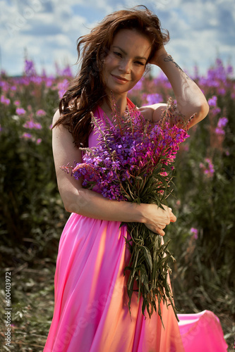 Smiling young woman with dark long hair holding the bouquet of pink flowers. Pink Ivan Tea or blooming Sally in the field