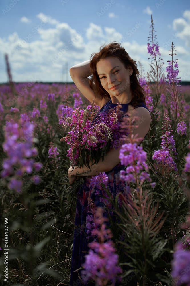 Smiling young woman with dark long hair holding the bouquet of pink flowers. Pink Ivan Tea or blooming Sally in the field Smiling young woman with dark long hair holding the bouquet of pink flowers. Pink Ivan Tea or blooming Sally in the field