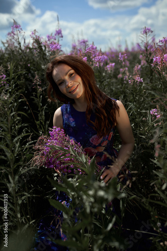 Smiling young woman with dark long hair holding the bouquet of pink flowers. Pink Ivan Tea or blooming Sally in the field