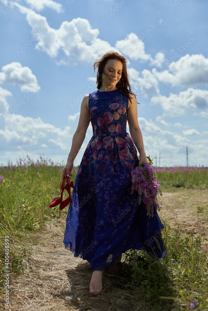 Young woman walking flowering field, turned away, gently touch yellow flowers. Brunette girl enjoys spring aromas, harmony. Backdrop dark clouds blue sky. Long hair fluttering wind. Denim sundress hat Young woman walking flowering field, turned away, gently touch yellow flowers. Brunette girl enjoys spring aromas, harmony. Backdrop dark clouds blue sky. Long hair fluttering wind. Denim sundress hat