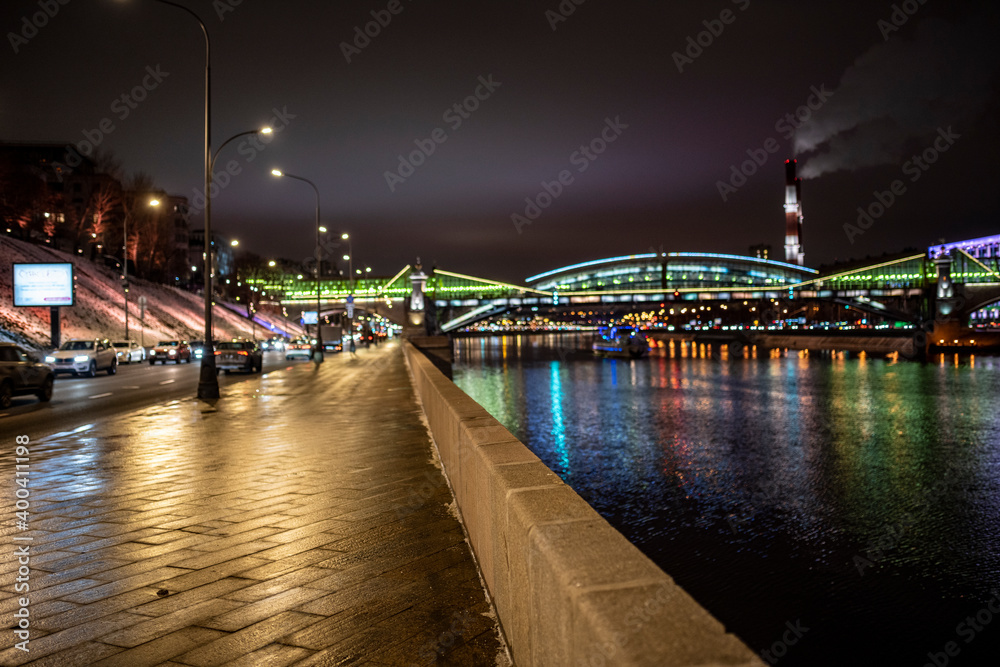 Fototapeta premium evening winter cityscape with river bridge and illuminated buildings