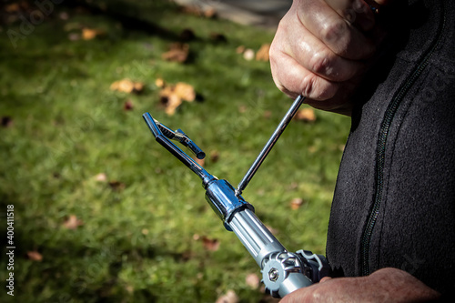 Man using screwdriver to attach a grabber attachment to a long pole outdoors with grass and fall leaves in background - closeup of hands - selective focus