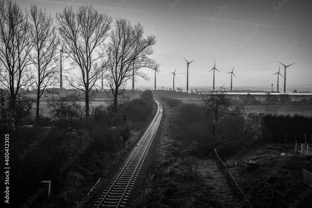 Railroad tracks lead to the horizon where some  wind turbines stand