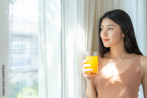 Beautiful beauty woman Asian cute girl feel happy drinking orange juice for good health in the morning , enjoying time in her home white bedroom background - lifestyle beauty woman concept