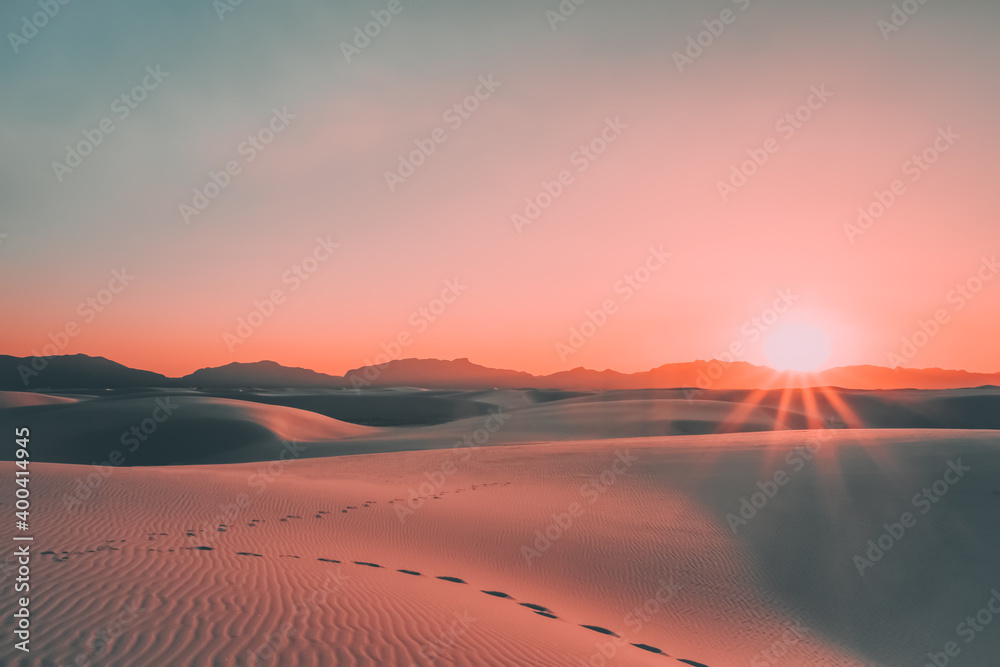 Sunburst above footprints in the gypsum sand dunes during a beautiful, vibrant sunset in White Sands National Park, New Mexico, USA. Sunburst above footprints in the gypsum sand dunes during a beautiful, vibrant sunset in White Sands National Park, New Mexico, USA.