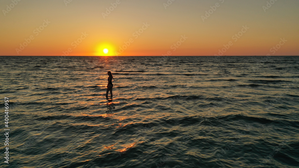 silhouette of a relaxed young girl in a bathing suit in the sea at sunrise. Happy Vacation Holiday Concept.