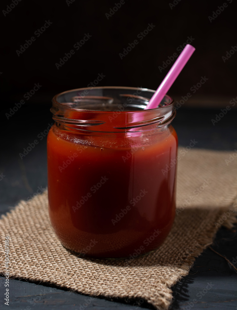 a jar of tomato juice with a straw on a sackcloth against a dark background. concept of rustic life, healthy food. a jar of tomato juice with a straw on a sackcloth against a dark background. concept of rustic life, healthy food.