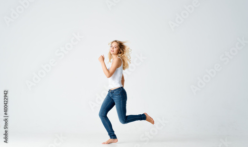 a slender woman in jeans and a white T-shirt barefoot on a light background in full growth