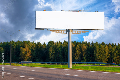 Big empty mockup Billboard along a highway with forest on background of blue sky with beautiful clouds.