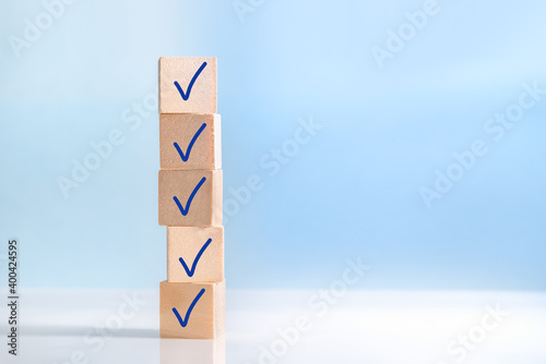 Check mark on wooden blocks, blue background with copy space. Checklist concept © olmax1975