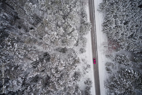A road in a winter spruce forest. A red car is driving along a snow-covered road. shooting from a drone. © ROMAN DZIUBALO