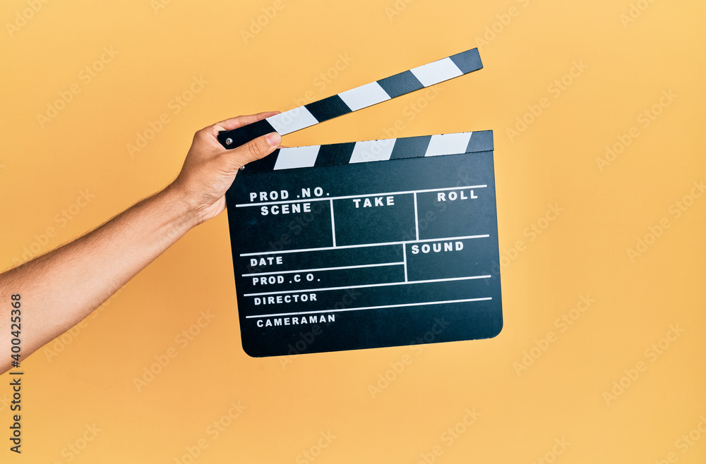 Hand of hispanic man holding movie clapboard over isolated yellow background.