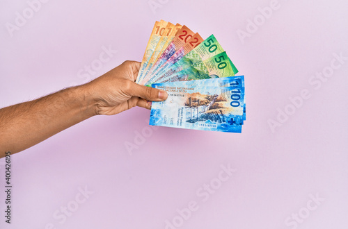 Hispanic hand holding swiss franc banknotes over isolated pink background. photo