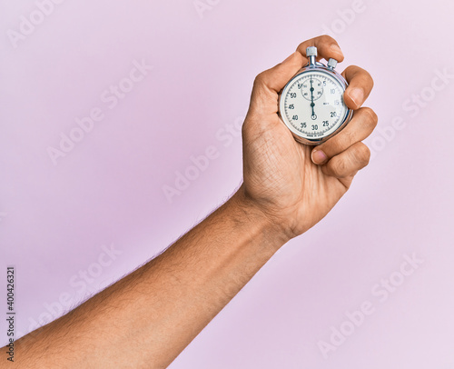 Hand of young hispanic man using stopwatch over isolated pink background.