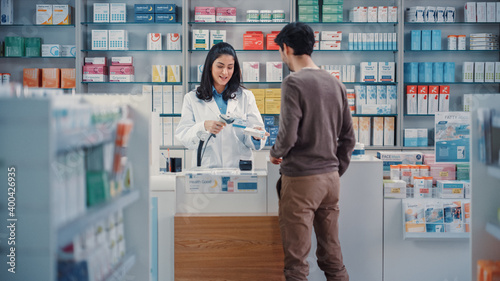 Pharmacy Drugstore Checkout Cashier Counter: Beautiful Female Pharmacist Scans Barcode and Handsome Young Man Talks to a Cashier and Pays for the Health Care Products at the Checkout Counter. photo