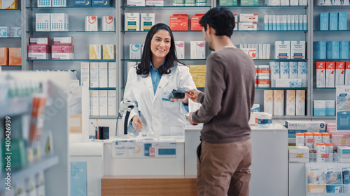 Fotografie Pharmacy Drugstore: Man Chooses Medicine, Comes to the Counter, Talks to Beautif