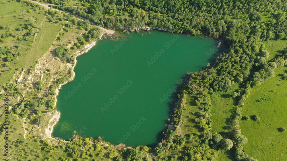 Aerial Drone view of colorful top of the trees and a lake at summer. A beautiful round lake in the middle of green space.
