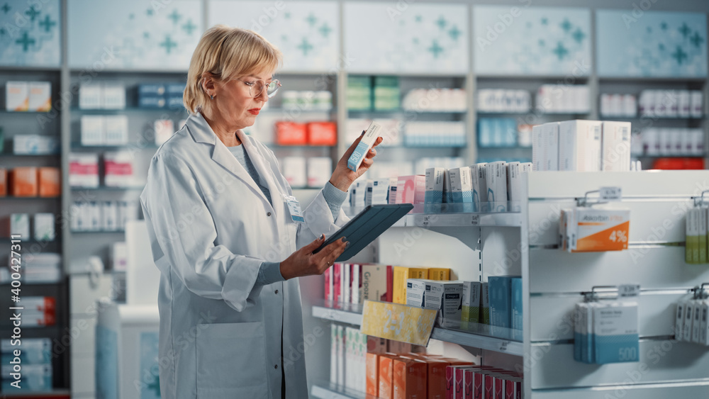 Pharmacy Drugstore: Mature Experienced Female Farmacist Uses Digital Tablet Computer to Arrange, Inventory, Check Medicine, Drugs, Vitamins on a Shelf. Medical Professional in Pharma Shop