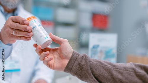 Pharmacy Drugstore Checkout Cashier Counter: Latin Mature Pharmacist Passes Box with Vitamins to a Young Male Customer. He is Buying Prescription Medicine. Close-up Shot with Focuse on Hands.