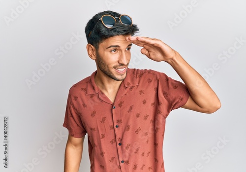 Young handsome man wearing casual summer clothes very happy and smiling looking far away with hand over head. searching concept.