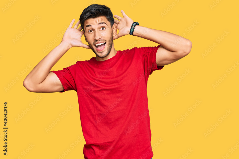 Young handsome man wearing casual red tshirt smiling cheerful playing peek a boo with hands showing face. surprised and exited Young handsome man wearing casual red tshirt smiling cheerful playing peek a boo with hands showing face. surprised and exited