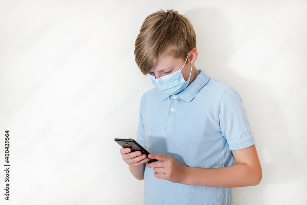boy in protective face mask plays on smartphone in online game. schoolboy watches homework on phone during coronavirus quarantine boy in protective face mask plays on smartphone in online game. schoolboy watches homework on phone during coronavirus quarantine