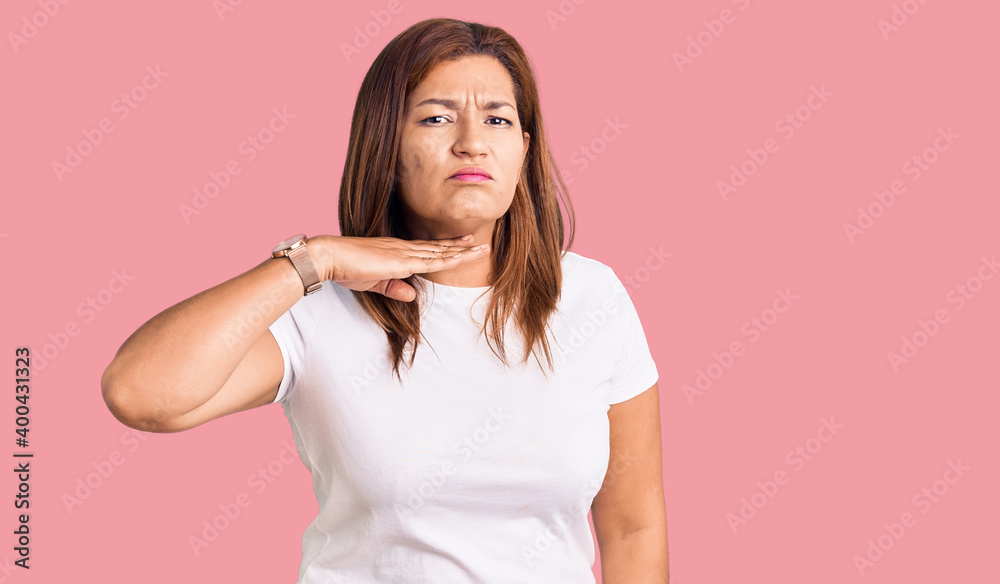 Middle age latin woman wearing casual white tshirt cutting throat with hand as knife, threaten aggression with furious violence Middle age latin woman wearing casual white tshirt cutting throat with hand as knife, threaten aggression with furious violence