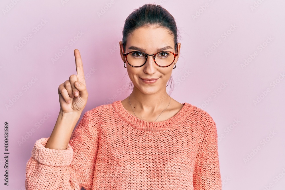 Young caucasian woman wearing casual clothes and glasses showing and pointing up with finger number one while smiling confident and happy. Young caucasian woman wearing casual clothes and glasses showing and pointing up with finger number one while smiling confident and happy.