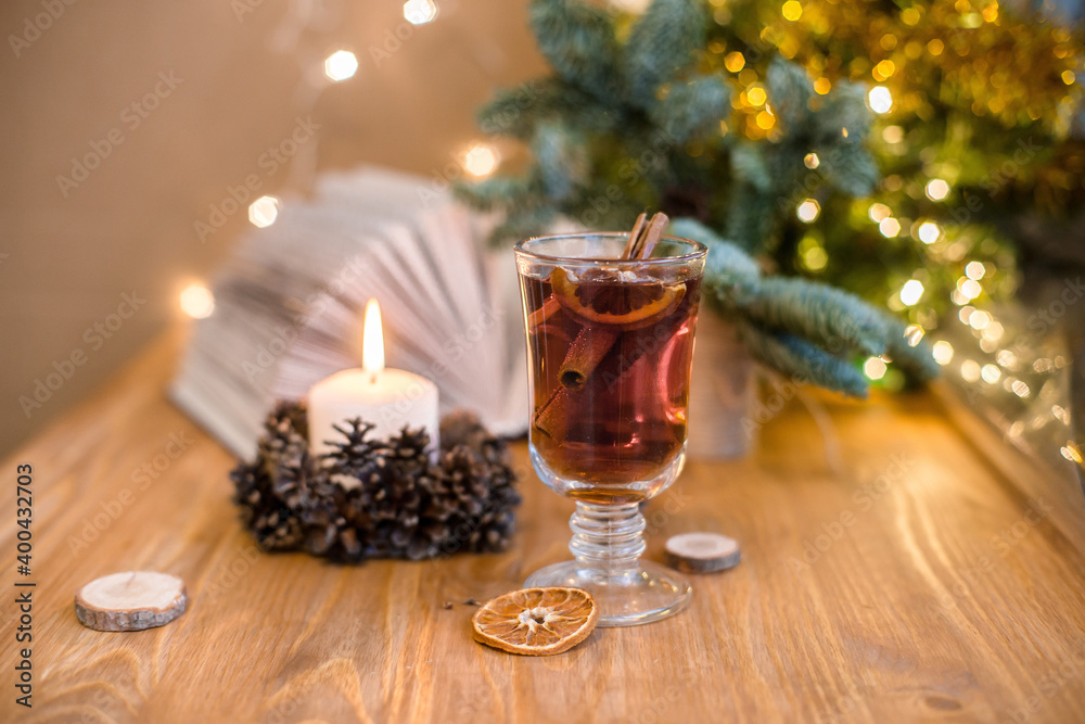 Mulled wine with cinnamon sticks and orange on a wooden table. Burning candle and Christmas tree lights Mulled wine with cinnamon sticks and orange on a wooden table. Burning candle and Christmas tree lights