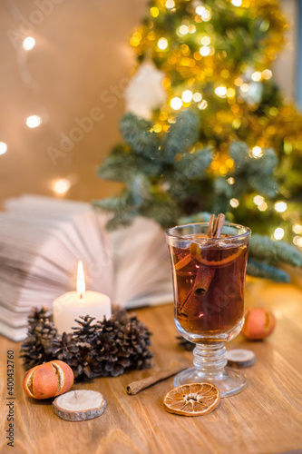 Mulled wine with cinnamon sticks and orange on a wooden table. Burning candle and Christmas tree lights