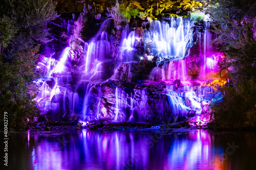 Waterfall in neon color. Flowing water illuminated by multicolored light. Night landscape with a colorful waterfall near the river