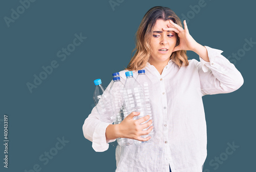Young caucasian woman holding recycling plastic bottles stressed and frustrated with hand on head  surprised and angry face