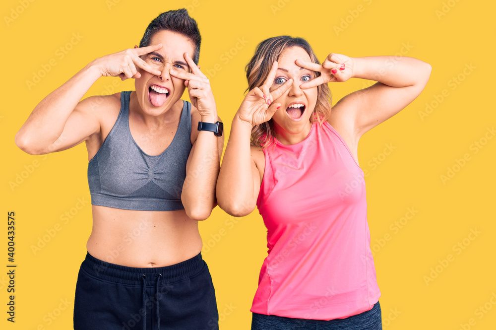 Couple of women wearing sportswear doing peace symbol with fingers over face, smiling cheerful showing victory Couple of women wearing sportswear doing peace symbol with fingers over face, smiling cheerful showing victory