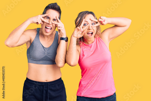 Couple of women wearing sportswear doing peace symbol with fingers over face, smiling cheerful showing victory