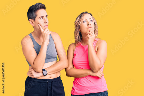 Couple of women wearing sportswear with hand on chin thinking about question, pensive expression. smiling with thoughtful face. doubt concept.