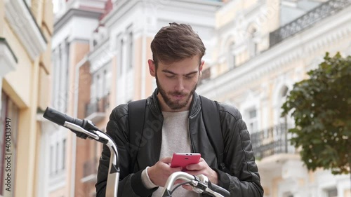 Young man stands on the street with bicycle and looks in his smartphone. Then he read the good news and takes violent emotions, joy and glee. Then he talks on smartphone photo