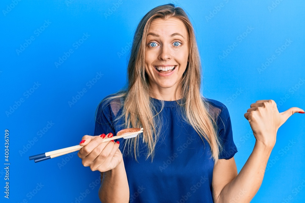 Beautiful caucasian woman eating nigiri sushi using chopsticks pointing thumb up to the side smiling happy with open mouth Beautiful caucasian woman eating nigiri sushi using chopsticks pointing thumb up to the side smiling happy with open mouth